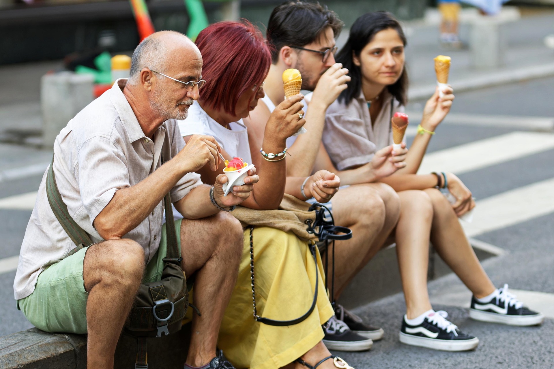 Reisegruppe beim Eisessen in der Stadt Vier Personen einer Reisegruppe sitzen entspannt am Straßenrand und genießen Eis, mit fröhlicher, sommerlicher Stimmung in urbaner Umgebung.