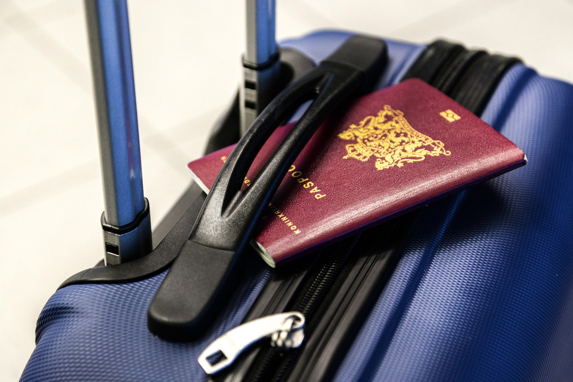 Reisepass auf Koffer am Flughafen Bordeauxroter Reisepass liegt auf einem blauen Rollkoffer mit ausgezogenem Griff, bereit für die Reise – Symbol für Urlaub und Aufbruch.