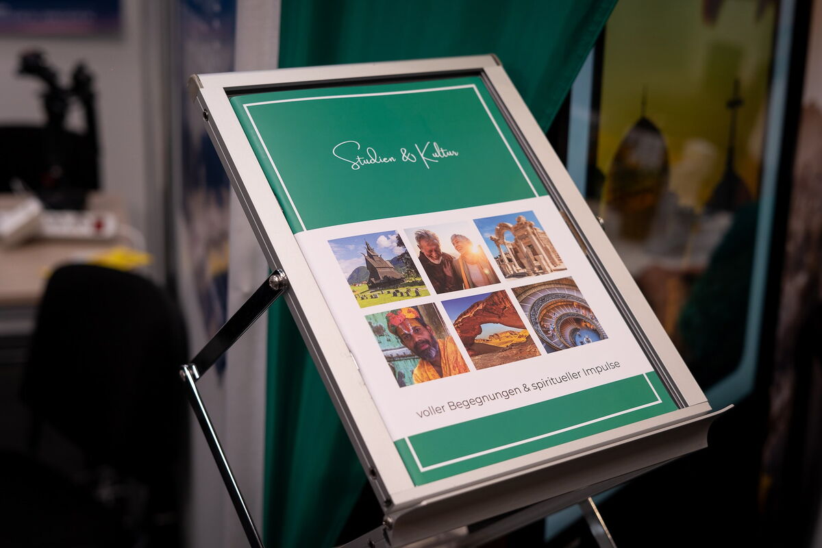 Reisekatalog „Spuren & Klänge“ auf einem Metallständer, mit Coverbildern von Reisezielen und Menschen