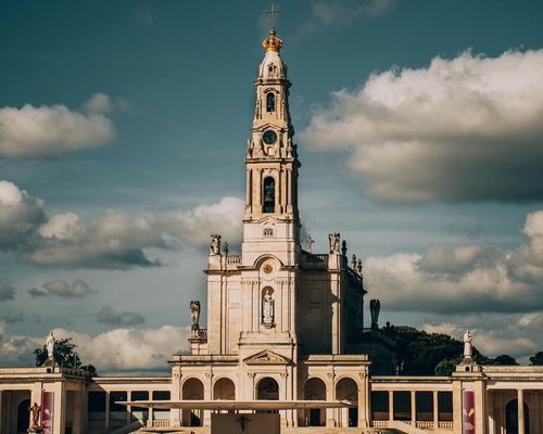 Frontansicht der Basilika Nossa Senhora do Rosário in Fátima unter einem teils bewölkten Himmel, mit symmetrischem Vorplatz und zentralem Glockenturm.